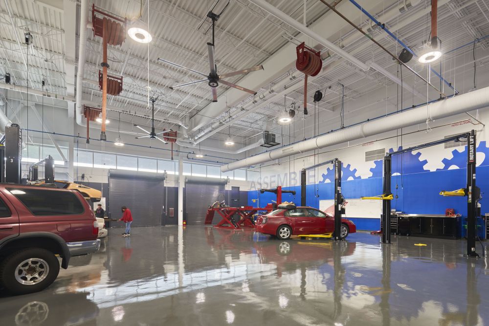 A large indoor garage space with several stations with cars and other vehicles that are used for training the students. The wall features a large mural with text and silhouettes and of gears.